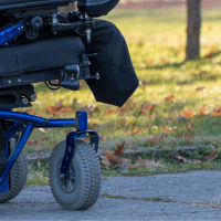 person in motorized wheelchair on sidewalk with grass and trees in background
