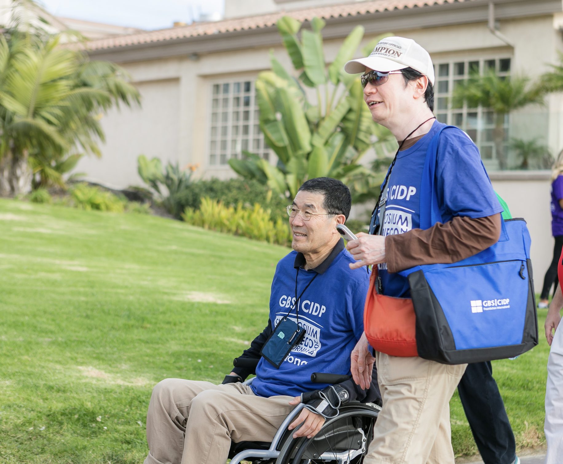 Two people, one in a wheelchair and one walking, in a garden.